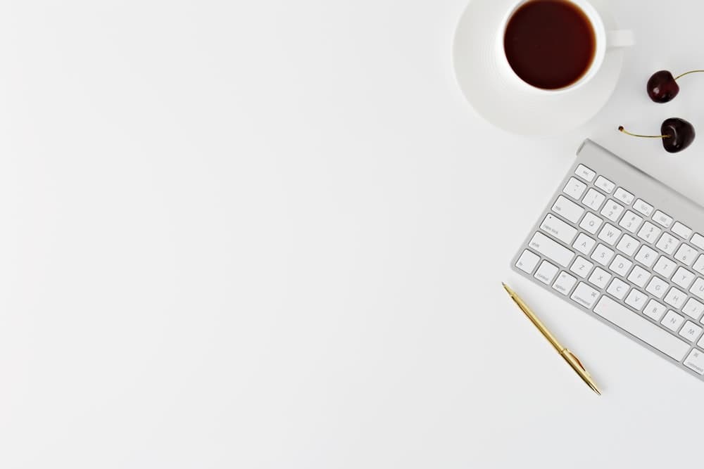 Minimal white workspace with laptop, keyboard, and coffee cup